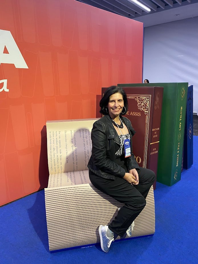Claudia Turatti sentada em um banco em forma de livro gigante, na feira Educa